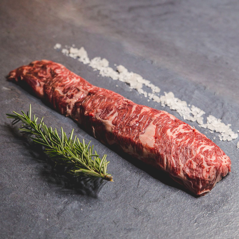 Macelleria Filetto di manzo crudo su sfondo scuro con un rametto di rosmarino e grani di sale grosso a lato